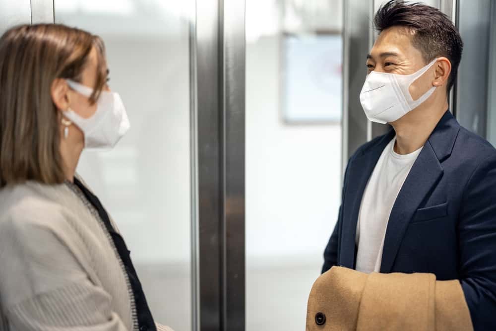 Young professionals wearing face masks greet each other in the elevator