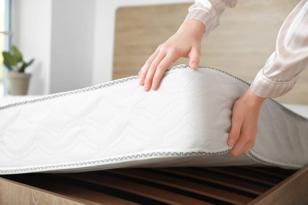 Woman putting a soft mattress on the bed.